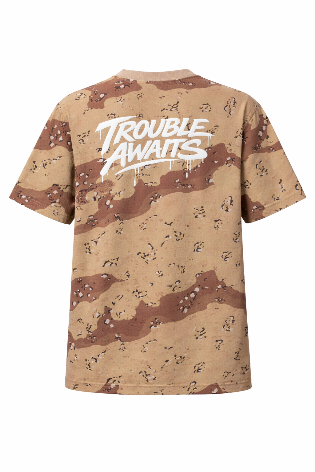 A back view of an oversized, boxy short-sleeve T-shirt displayed flat against a neutral gray background. The shirt features a desert camouflage pattern made up of light tan, sandy beige, and medium brown shapes with small scattered darker markings. Centered across the upper back is a large, bold graphic reading “Trouble Awaits” in a stylized graffiti-inspired script. The lettering is white with a slightly glossy appearance and includes dripping paint details extending downward from several letters.
