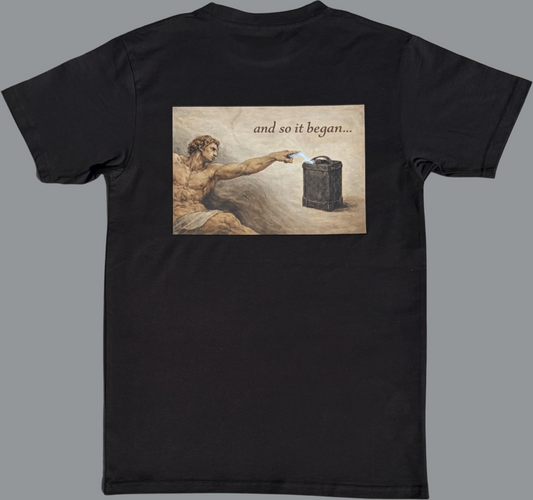 Black short sleeve t-shirt featuring a rectangular graphic printed across the upper back. The image is styled like a classical painting and shows a muscular figure reaching out with an extended hand toward a battery-like object, with a small spark of electricity between them. Above the image, the text reads “and so it began…”. The rest of the shirt is plain black with no additional visible graphics.
