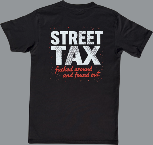 Black short sleeve t-shirt featuring a large graphic printed across the upper back. The design includes the words “STREET TAX” in bold white capital letters with a distressed texture. Below it, in smaller red script, the text reads “fucked around and found out.” The graphic also includes red paint splatter accents around the text. The rest of the shirt is plain black.