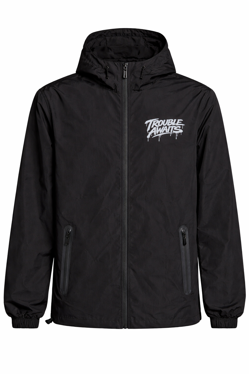 ront-facing ghost mannequin image of a black hooded windbreaker jacket. The jacket features a full-length front zipper, a structured hood, and a lightweight, slightly matte fabric. A small silver “Trouble Awaits” logo in a graffiti-style font is printed on the left chest. Two vertical zippered pockets with waterproof-style trims sit on either side of the front. The sleeves are relaxed with elastic cuffs, and the hem appears adjustable, giving the jacket a clean, functional streetwear look.