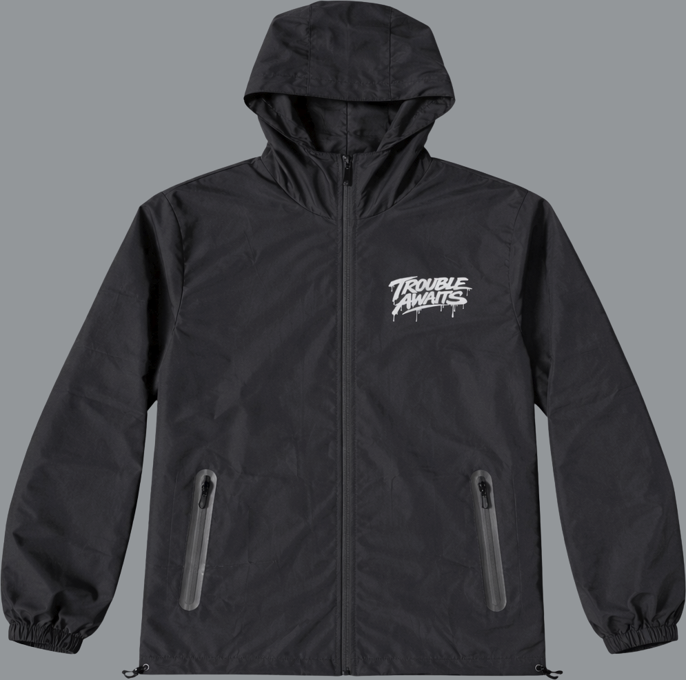 A dark gray to black lightweight hooded windbreaker jacket is shown from the back against a plain background. The jacket has a relaxed, slightly oversized fit with elastic cuffs and a gathered hem. The hood is up and structured. Centered across the upper back is a large, bold white graphic reading “Trouble Awaits” in a graffiti-inspired script font, featuring paint-drip details extending downward from the lettering. The fabric appears smooth and slightly matte with subtle creasing