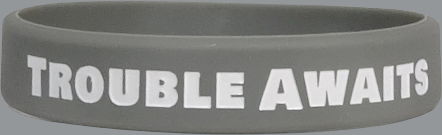 A single matte gray silicone wristband displayed against a plain gray background. The band features bold, uppercase white text reading “TROUBLE AWAITS” centered along the outer surface. The lettering is thick and highly legible, contrasting clearly with the darker gray band. The material appears smooth and flexible with a soft, rubber-like finish. The image is tightly cropped to focus on the wristband, with even lighting and minimal shadows for a clean, product-focused presentation.