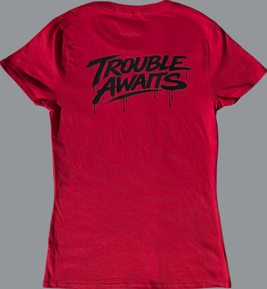 A back view of a women’s lightweight T-shirt in a rich red color, displayed against a neutral gray background. The shirt has a slightly fitted, tapered shape with short sleeves and a crew neckline.

Centered across the upper back is a bold black graphic reading “Trouble Awaits” in a stylized graffiti-inspired font with dripping paint details, giving it a streetwear aesthetic. The print sits across the shoulder blade area and contrasts sharply against the red fabric.

The fabric appears soft and lightweight 