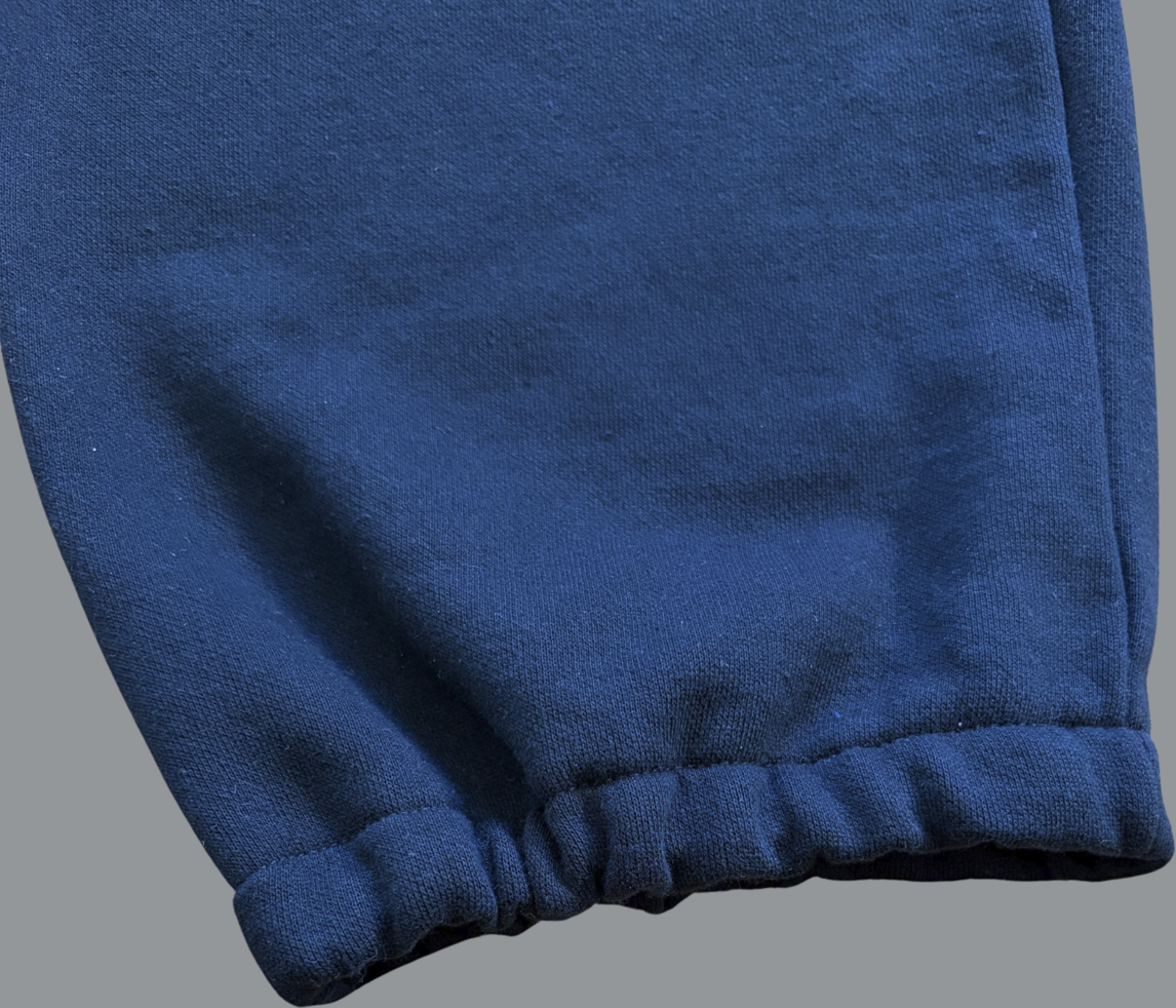 Close-up of the bottom leg of black sweatpants showing an elastic cuff. The fabric is slightly gathered at the ankle, creating a snug, tapered finish. The material appears soft and midweight with a smooth outer surface, and subtle creases are visible along the leg.