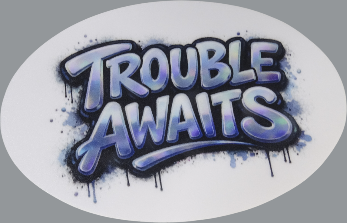 An oval-shaped sticker displayed against a neutral gray background. The design features the words “Trouble Awaits” in a bold, graffiti-style font with rounded, bubble-like lettering. The text has a soft gradient fill blending shades of blue, purple, and hints of green, giving it a slightly iridescent look. Surrounding the lettering is a dark, spray-paint-style outline with visible overspray and splatter effects, creating a street-art aesthetic. Paint drips extend downward from parts of the design