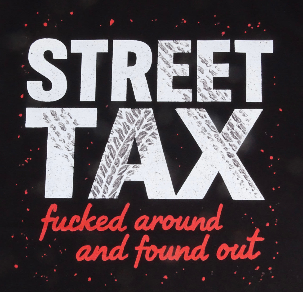 Featuring a large graphic printed across the upper back. The design includes the words “STREET TAX” in bold white capital letters with a distressed texture. Below it, in smaller red script, the text reads “fucked around and found out.” The graphic also includes red paint splatter accents around the text.